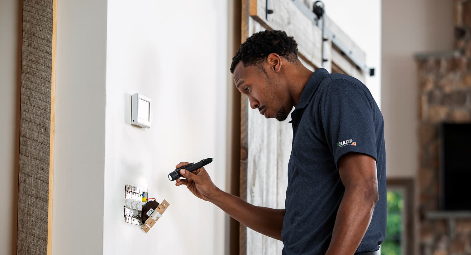 A professional Harp electrician using a flashlight to safely inspect and troubleshoot exposed residential wall switch wiring during an electrical repair service.