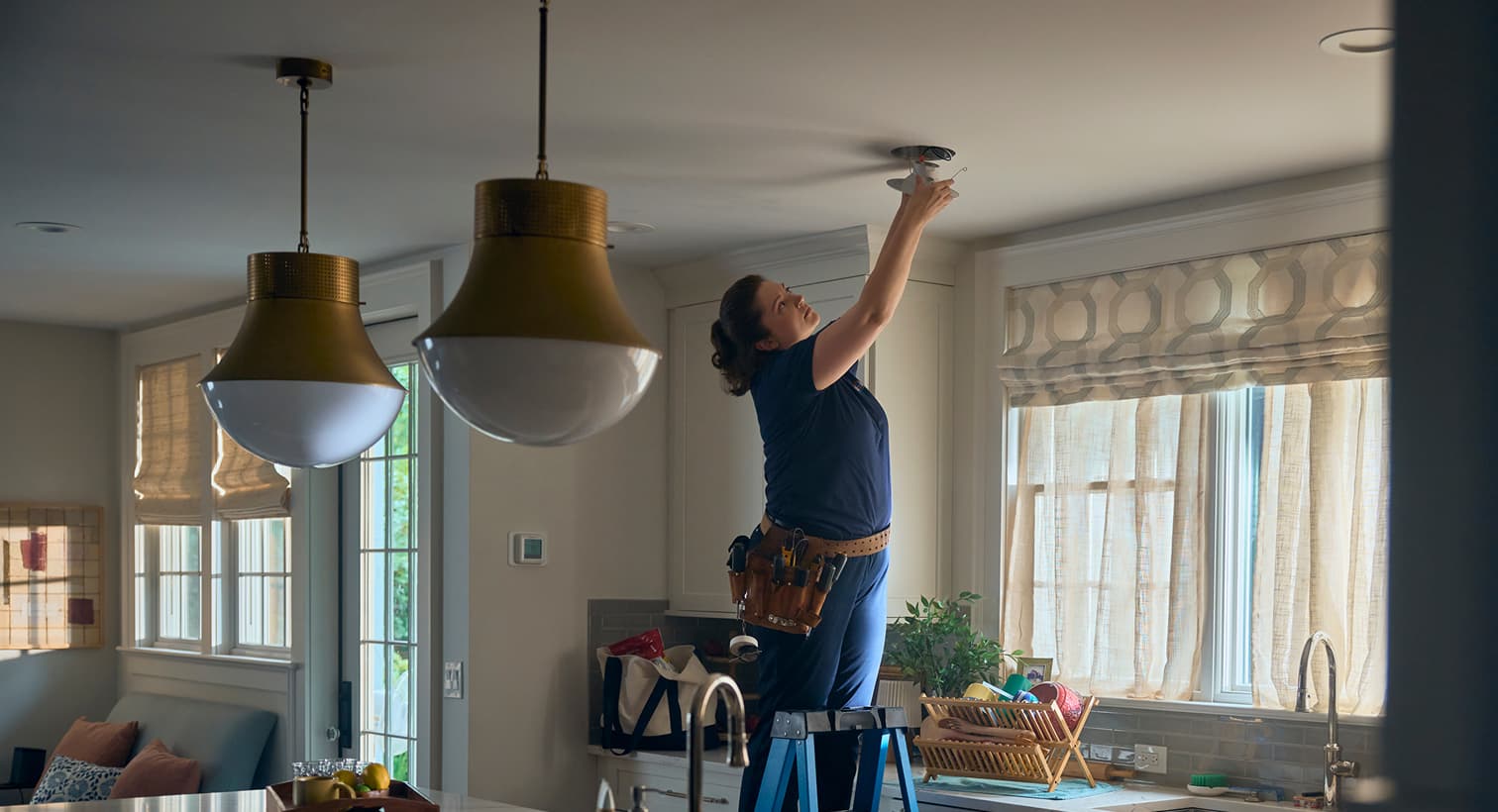 A professional Harp electrician standing on a ladder to install modern recessed ceiling lights during a residential electrical installation service.