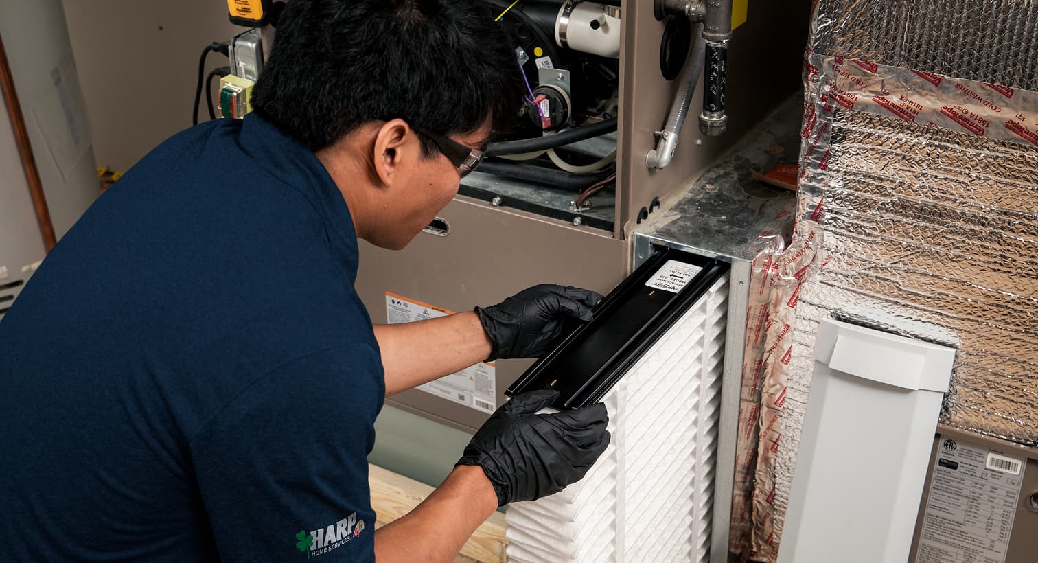 A professional Harp HVAC technician replacing a clean pleated air filter in an indoor air handler unit during a routine AC maintenance tune-up.