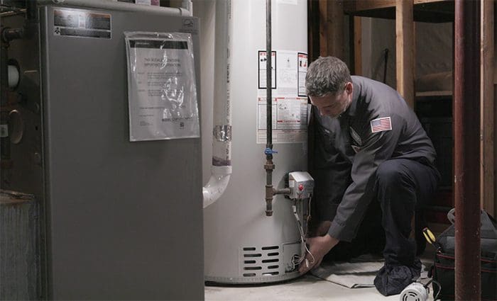 A HARP Home Services performing hot water heater repair in a house basement and preparing for water heater replacement