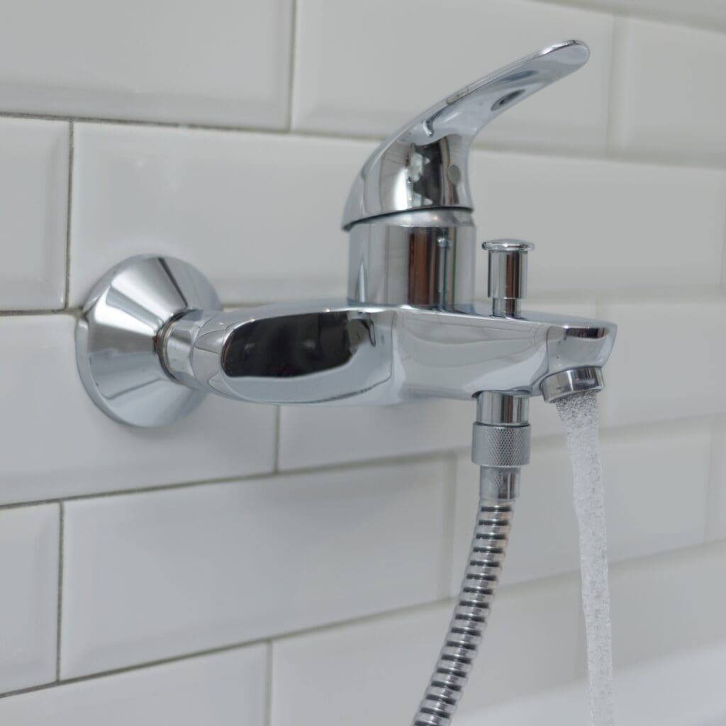 Close-up of an open chrome faucet mixer in bathtub with running water.