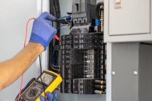 Electrician is using a digital meter to measure the voltage at the circuit breaker control cabinet on the wall.